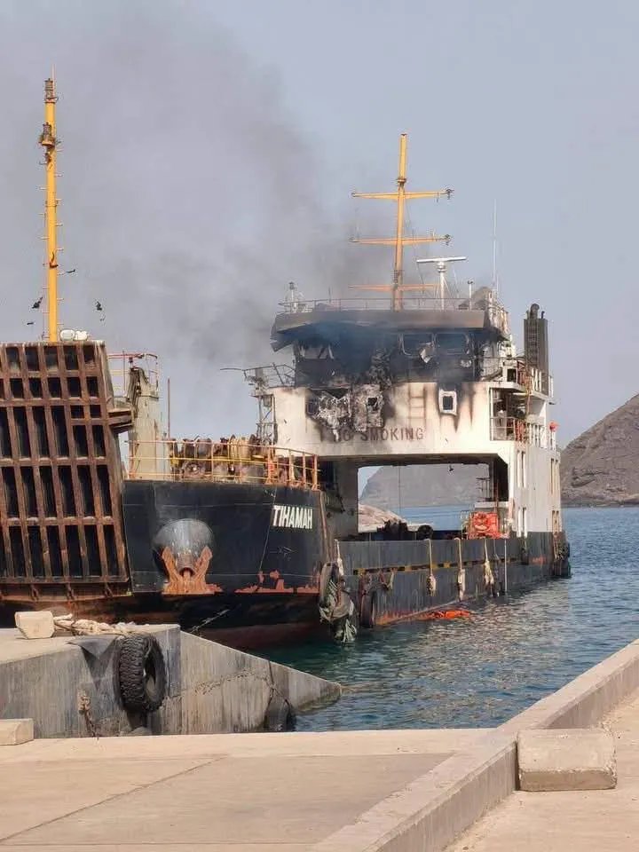 The cargo ship Tihamah moored at the quay in Al-Makha port, Yemen, her bridge and superstructure blackened by fire and black smoke still rising behind her.
